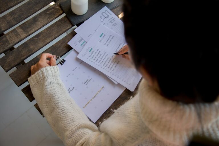 Person reviewing an insurance policy, payment notice, and calendar beside a laptop at a kitchen table.